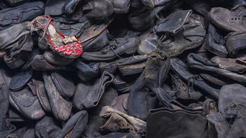 Unzählige dunkle Schuhe auf einem Haufen, ein roter Schuh liegt oben drauf. Es sind Schuhe in der Gedenkstätte Auschwitz-Birkenau.