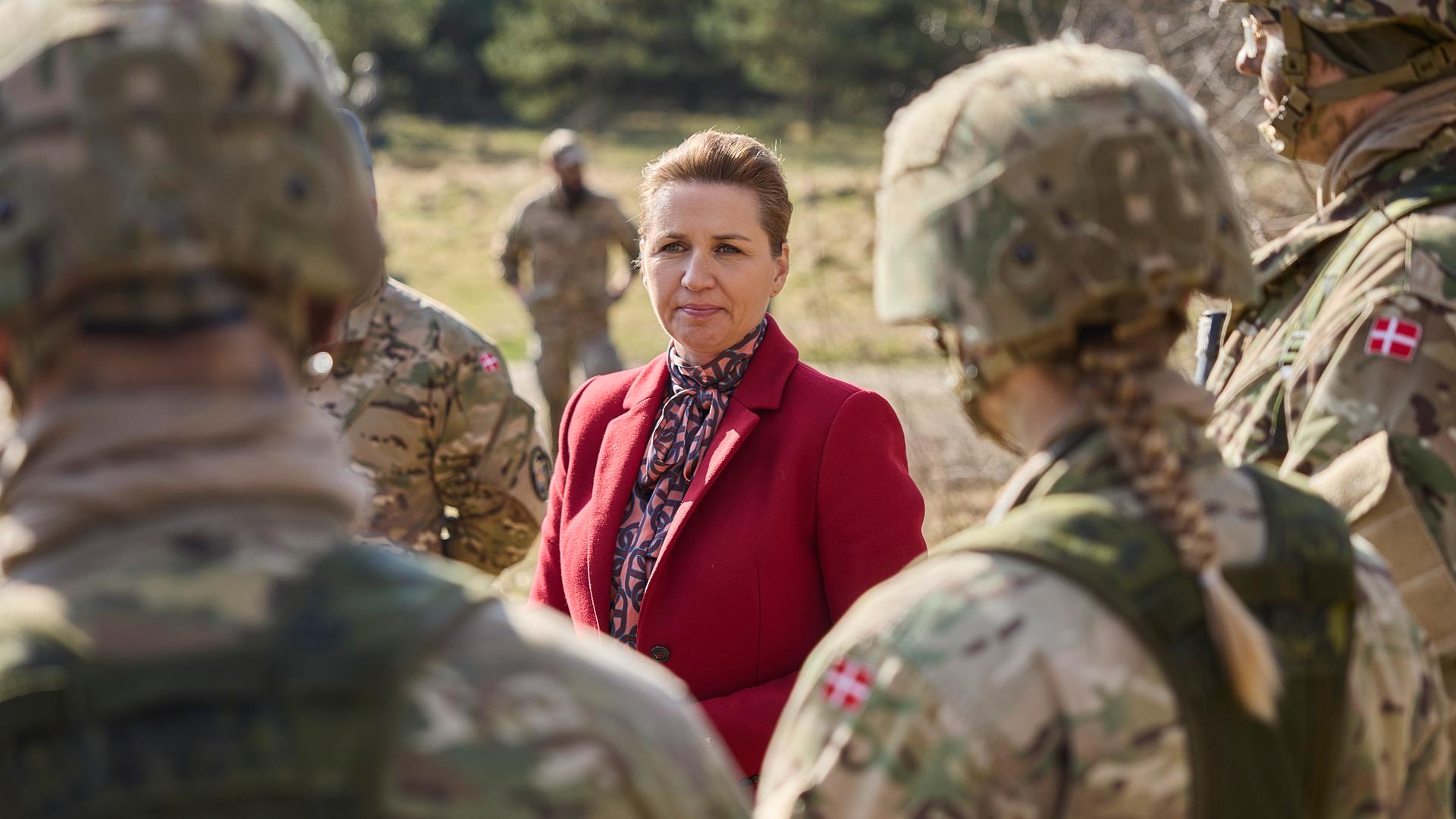 Ministerpräsidentin Mette Frederiksen unterhält sich mit Soldaten der dänischen Armee. Unter ihnen ist auch eine Frau. Ihr Zopf lugt unter ihrem Helm hervor. 