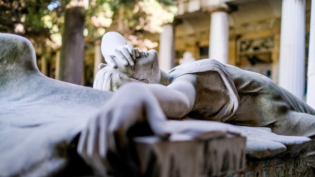 Statue eines liegenden Engels, der sich eine Hand vors Gesicht hält, auf einem Grab