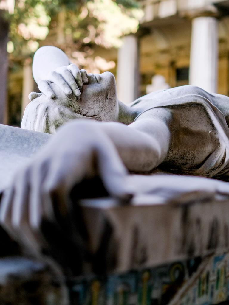 Statue eines liegenden Engels, der sich eine Hand vors Gesicht hält, auf einem Grab