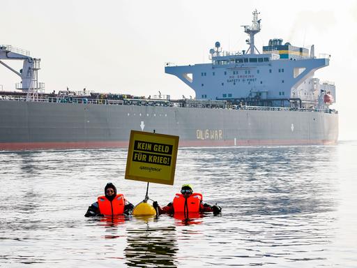 Aktivisten der Umweltorganisation Greenpeace demonstrieren in der Ostsee vor einem Schiff, das russisches Öl transportiert. Auf einem Plakat steht: Kein Geld für Krieg. 