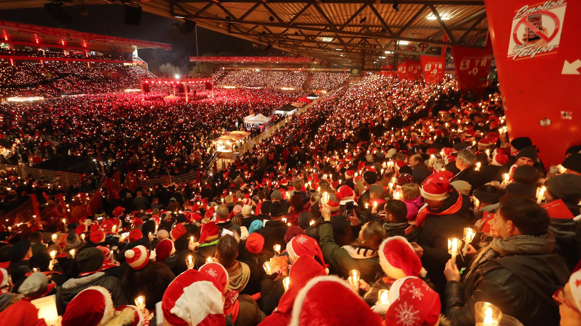 Tausende Fans mit Kerzen in der Hand und roten Mützen auf dem Kopf nehmen am Weihnachtssingen im Stadion des 1.FC Union Berlin teil. Tausende Fans mit Kerzen in der Hand und roten Mützen auf dem Kopf nehmen am Weihnachtssingen im Stadion des 1.FC Union Berlin teil.