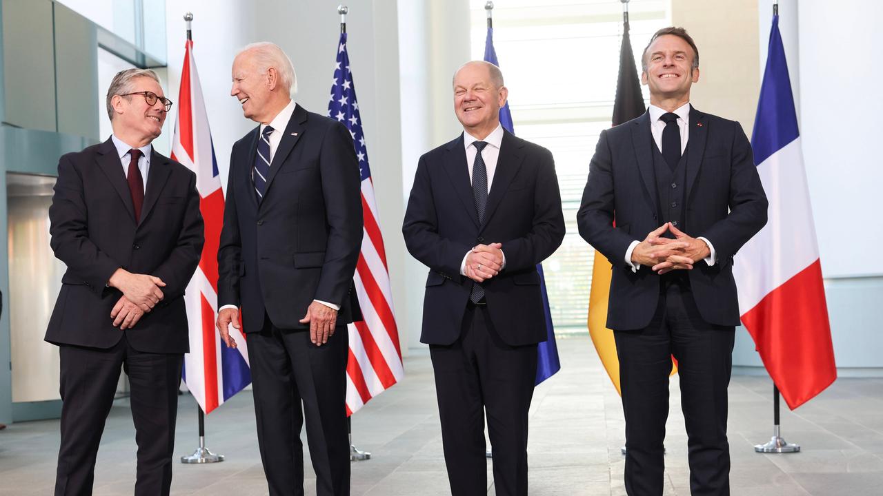 Der britische Premierminister Keir Starmer, US-Präsident Joe Biden, der französische Staatspräsident Emmanuel Macron und Bundeskanzler Olaf Scholz posieren lächelnd für ein Foto. Hinter ihnen die Landesflaggen.