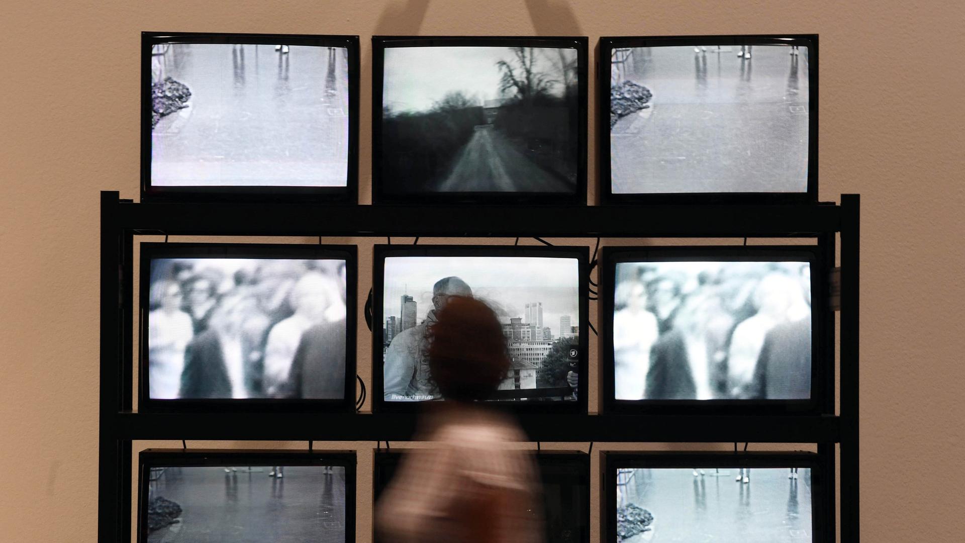 11.07.2018, Baden-Württemberg, Karlsruhe: Eine Besucherin des Karlsruher Zentrums für Kunst und Medien (ZKM) geht an der Installation "Wipe Cycle" aus den Jahren 1969/2017 von Frank Gilette und Ira Schneider vorbei. Die Arbeit ist Teil der Ausstellung "Kunst in Bewegung. 100 Meisterwerke mit und durch Medien. Ein operationaler Kanon" die vom 14.07.2018 bis zum 10.02.2019 zu sehen war. Es handelt sich um neun aufeinander gestapelte Fernsehapparate mit schwarz-weißen Bildern.
