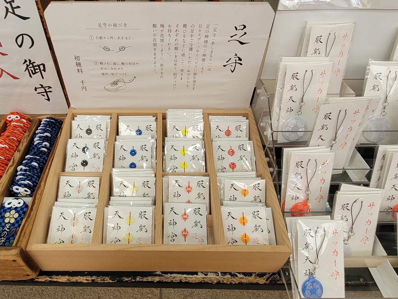 Amulette für Laufsportler, beschrieben mit japanischen Schriftzeichen, werden in einer Holzkiste angeboten.