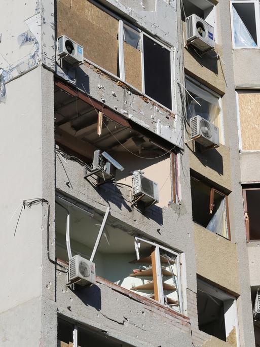 Die Fenster und Balkone eines Wohnhauses wurden mit Brettern verschlagen. Viele Fenster sind zerbrochen, vermutlich aufgrund von Druckwellen von Explosionen.