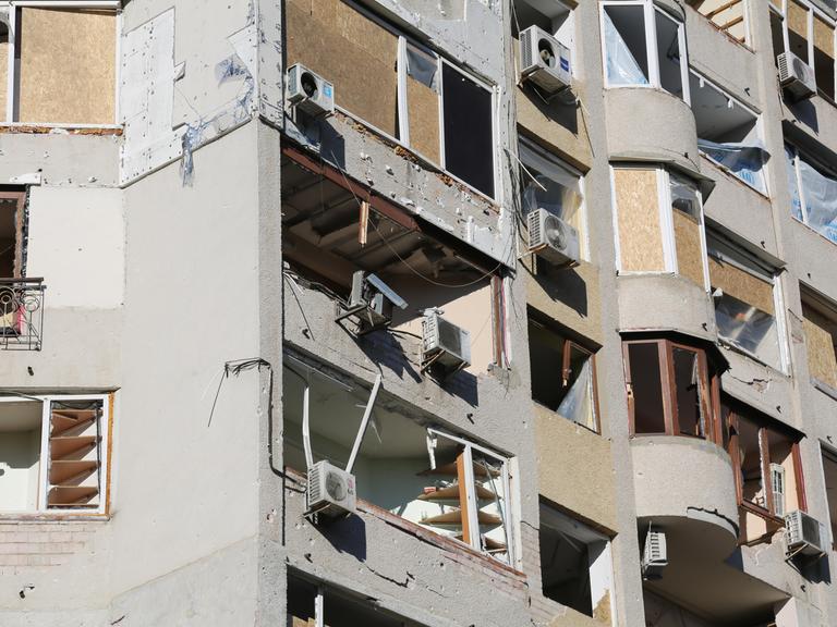 Die Fenster und Balkone eines Wohnhauses wurden mit Brettern verschlagen. Viele Fenster sind zerbrochen, vermutlich aufgrund von Druckwellen von Explosionen.