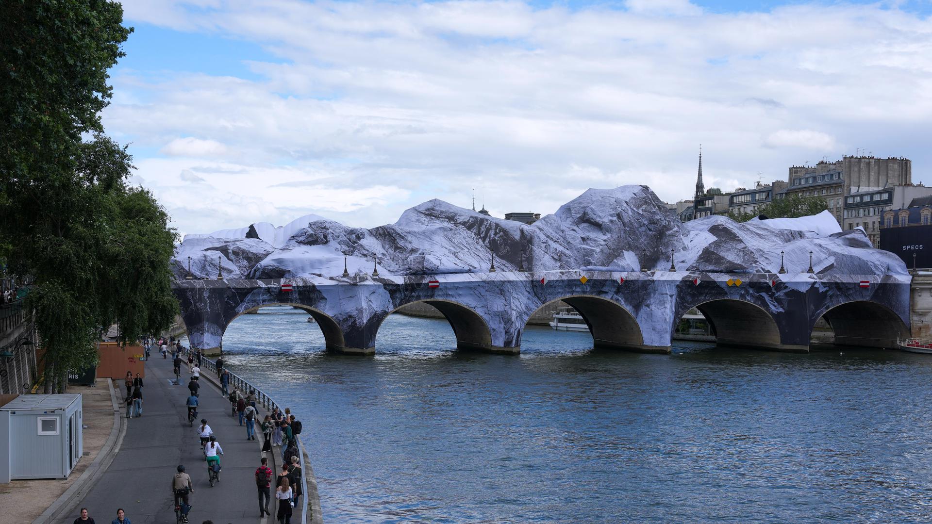 Fußgänger gehen in der Nähe der temporären Kunstinstallation „La Caverne du Pont Neuf“ (Die Höhle des Pont Neuf) auf der Brücke Pont Neuf in Paris. Fußgänger gehen in der Nähe der temporären Kunstinstallation „La Caverne du Pont Neuf“ (Die Höhle des Pont Neuf) auf der Brücke Pont Neuf in Paris.