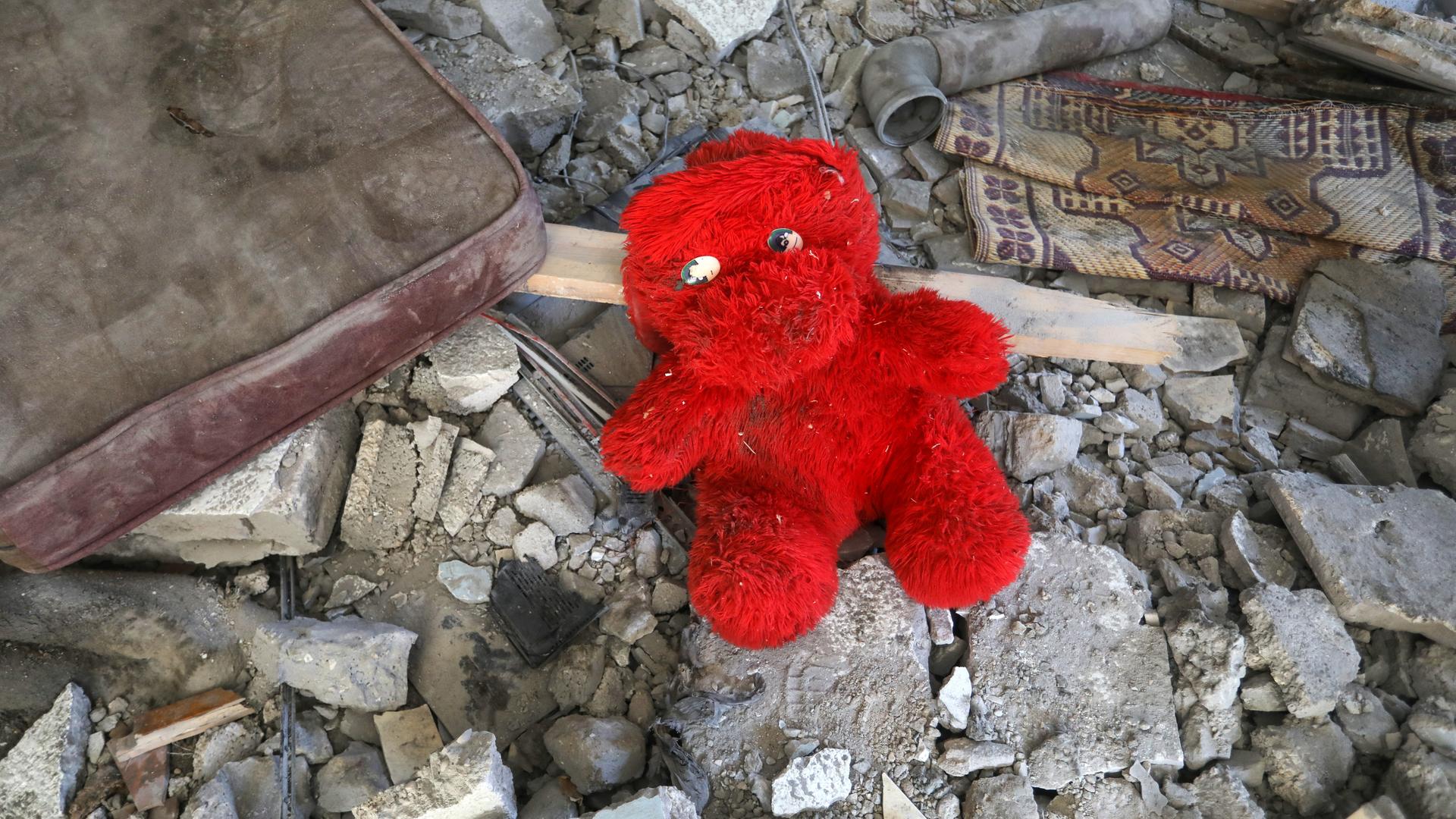 Ein rotes Plüschtier liegt auf Trümmern.