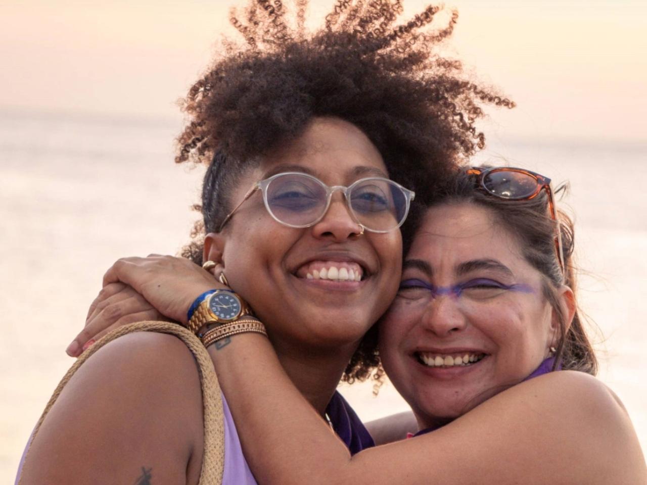 Eliana Toncel und Laura Chávez Herrera umarmen sich in der Bucht von Santa Marta und halten ein Schild mit "500 Jahre Widerstand".