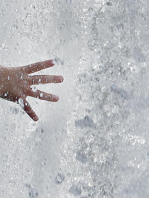 Das Bild zeigt eine Kinderhand, die bei bei Temperaturen um 31 Grad Celsius in eine Springbrunnenanlage mit sprudelndesm Wasser greift.