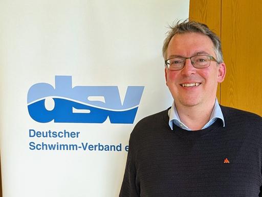 Portraitfoto von DSV-Präsident David Profit vor dem Logo des DSV