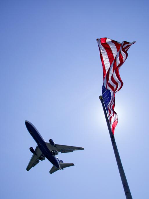 Untersicht auf ein Flugzeug am Himmel. Rechts im Bild die amerikanische Flagge. Untersicht auf ein Flugzeug am Himmel. Rechts im Bild die amerikanische Flagge.