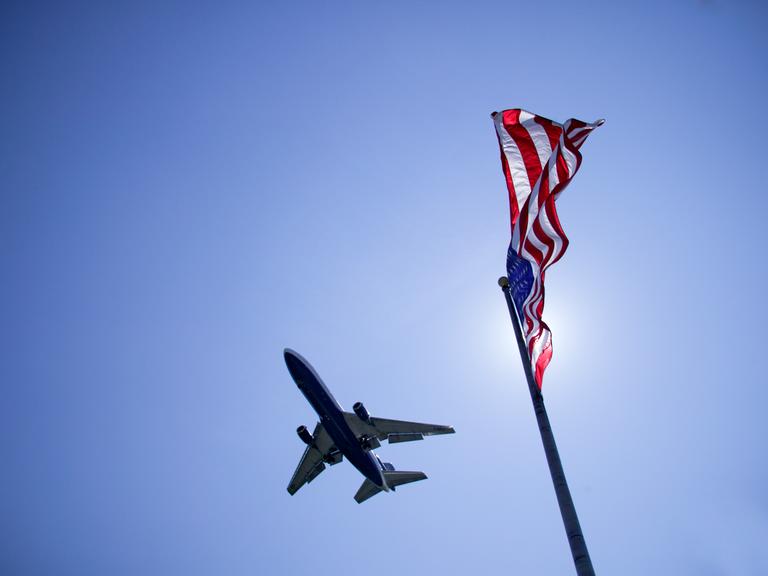 Untersicht auf ein Flugzeug am Himmel. Rechts im Bild die amerikanische Flagge. Untersicht auf ein Flugzeug am Himmel. Rechts im Bild die amerikanische Flagge.