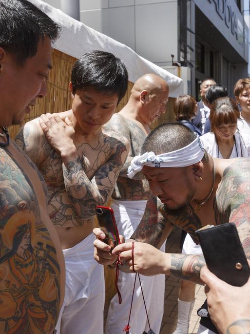 Männer mit Ganzkörpertätowierungen fotografieren ihre Tattoos bei einem Festival in Japan.