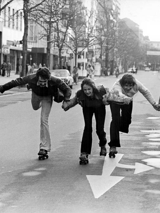 Fünf Menschen halten sich an den Händen und fahren Rollschuh auf einer leeren Straße.