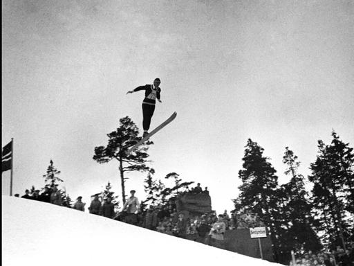 Eine historische Fotografie zeigt den Skispringer Jacob Tullin Thams wie er über einen Abhang fliegt.