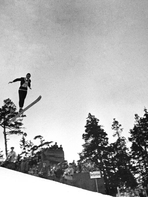 Eine historische Fotografie zeigt den Skispringer Jacob Tullin Thams wie er über einen Abhang fliegt.