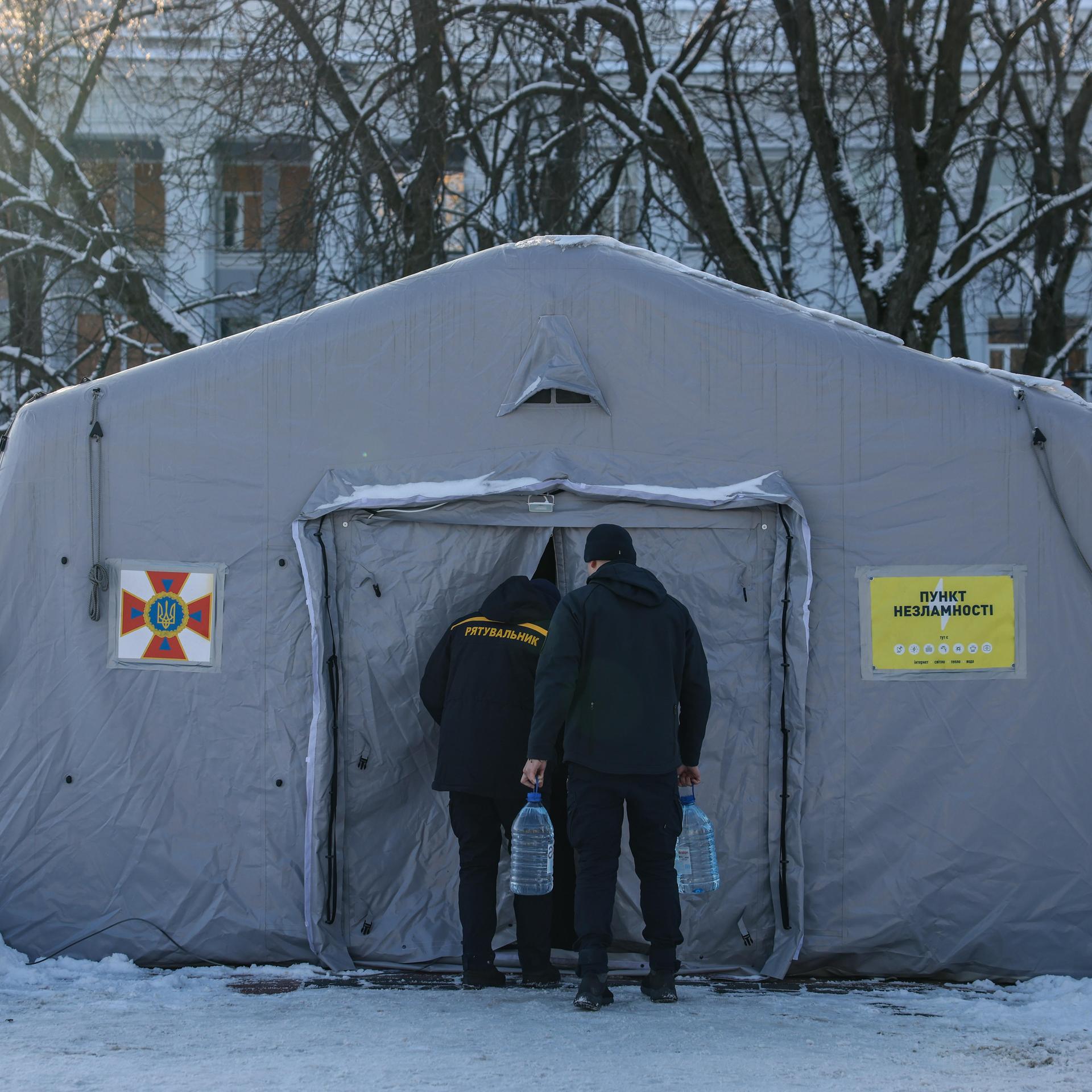 Zwei Männer gehen in ein großes, weißes Heizzelt, das von Schnee und Wohnhäusern umgeben ist.