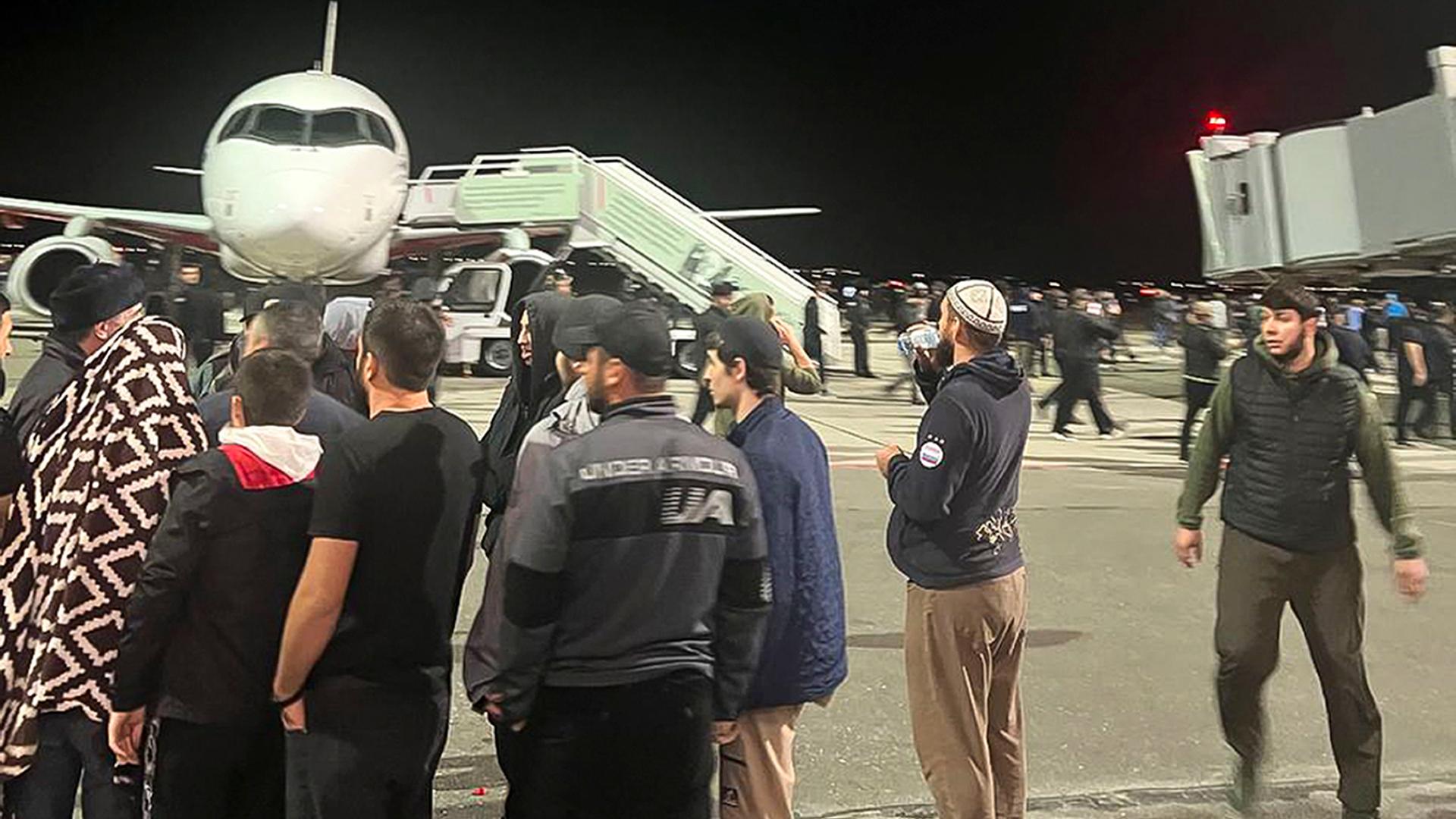 Menschen stehen auf dem Rollfeld am Flughafen Dagestan vor einer Maschine und rufen antisemitische Slogans.