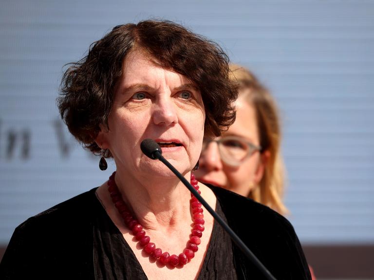 Die Autorin Regina Scheer trägt eine rote Halskette zur dunklen Bluse und spricht in ein Mikrofon.