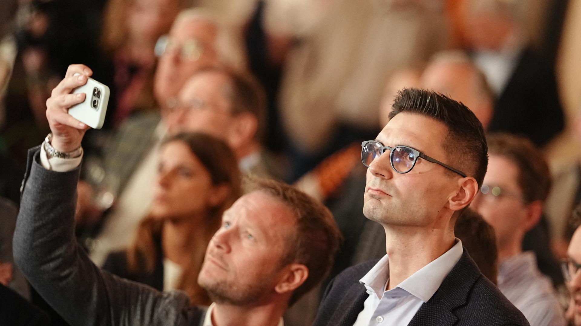 Ein mittelalter Mann mit kurzen dunklen Haaren steht bei einer Wahlveranstaltung zwischen lauter Menschen. 