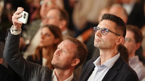 Ein mittelalter Mann mit kurzen dunklen Haaren steht bei einer Wahlveranstaltung zwischen lauter Menschen. 