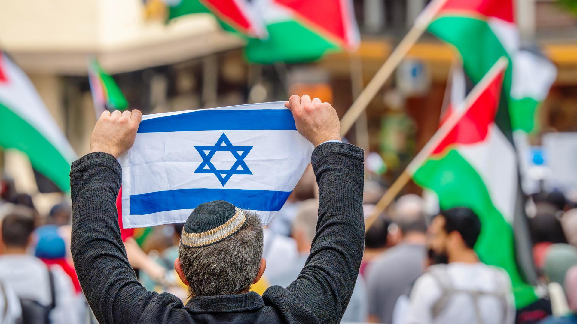 Ein Pro-Israel-Demonstrant hält einer Free-Palestine-Demonstration die israelische Flagge entgegen