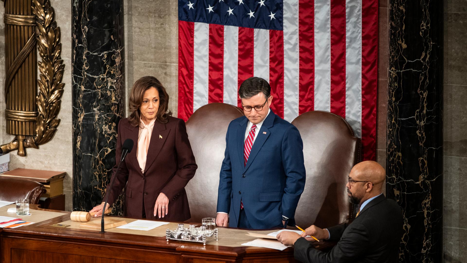 United States Vizepräsidentin Kamala Harris steht neben dem Sprecher der House of Representatives Mike Johnson am 6. Januar 2025. Im Hintergrund sieht man die Flagge der Vereinigten Staaten.