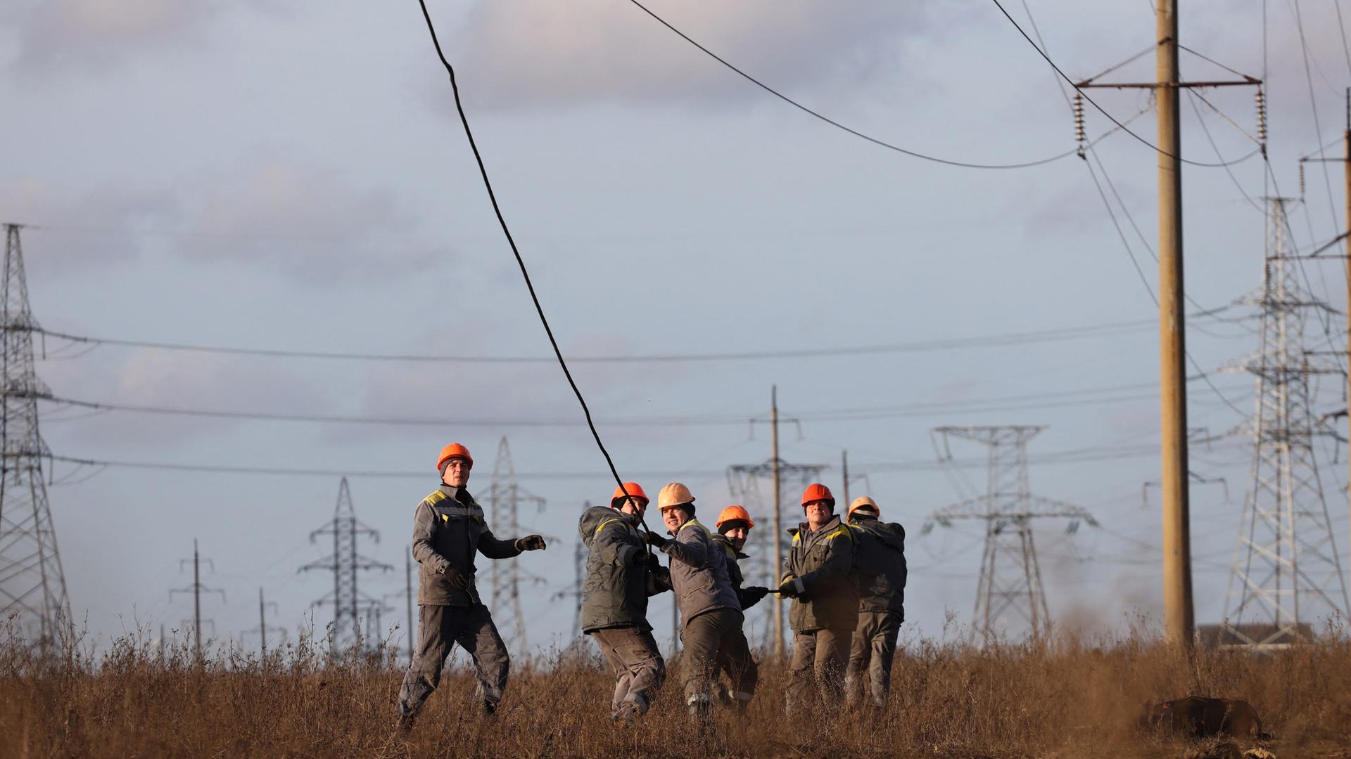 Arbeiter mit Helmen ziehen gemeinsam an einem kaputten Stromkabel, das von einem Strommast herunterhängt. Arbeiter mit Helmen ziehen gemeinsam an einem kaputten Stromkabel, das von einem Strommast herunterhängt.