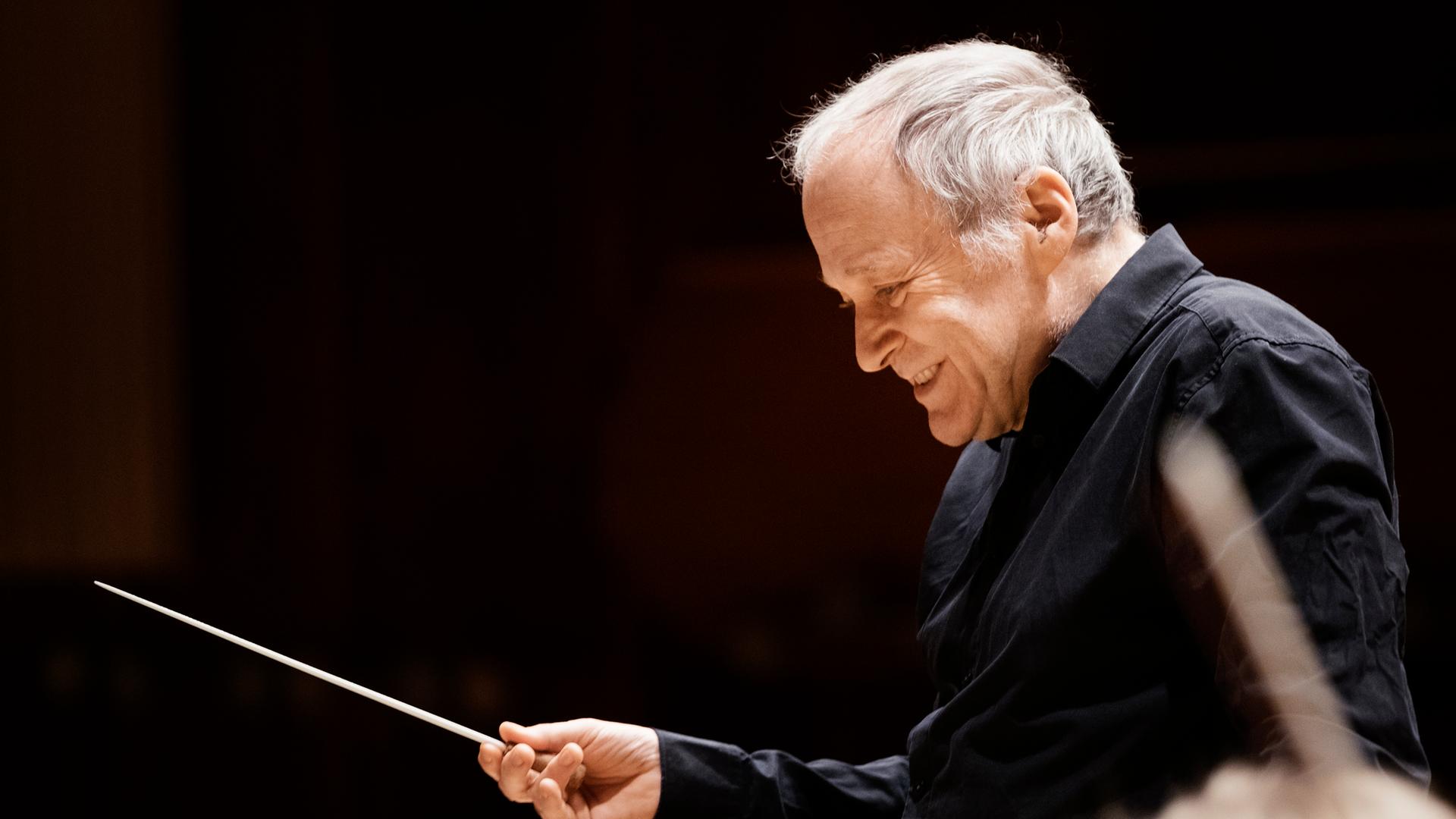 Adam Fischer dirigiert mit Stab vor einem Orchester.
