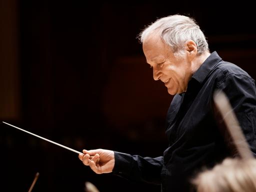 Adam Fischer dirigiert mit Stab vor einem Orchester.