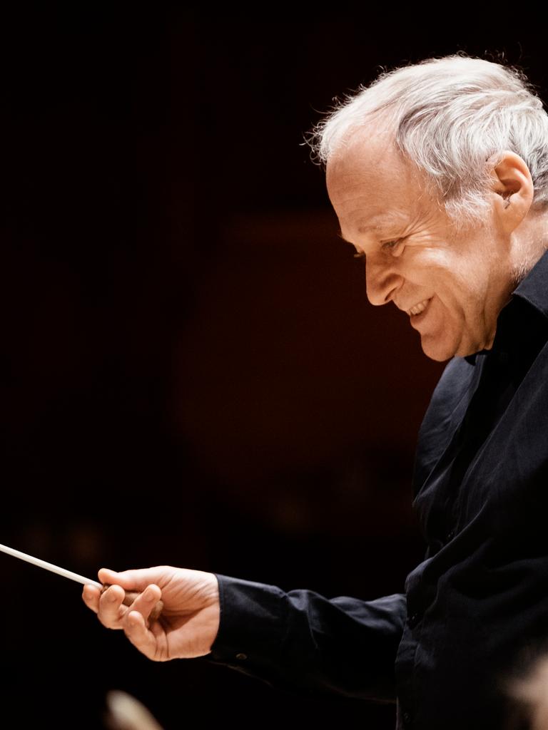 Adam Fischer dirigiert mit Stab vor einem Orchester.