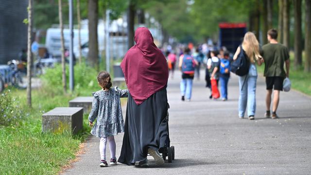 Eine muslimische Frau mit Kopf-Tuch hält ihre Tochter an der Hand und geht auf einem Gehweg.