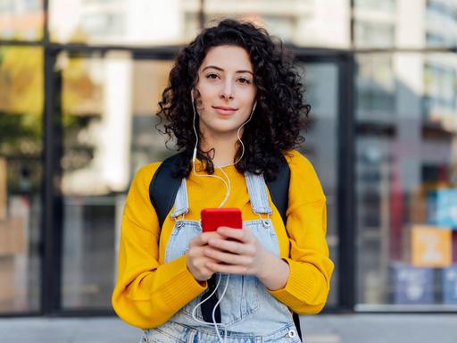 Eine junge Frau hat Kopfhörer auf, die mit ihrem Smartphone verbunden sind, das sie in der Hand hält