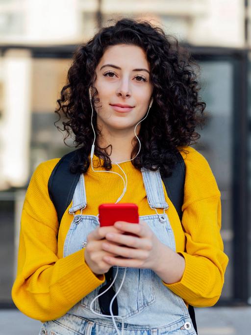 Eine junge Frau hat Kopfhörer auf, die mit ihrem Smartphone verbunden sind, das sie in der Hand hält