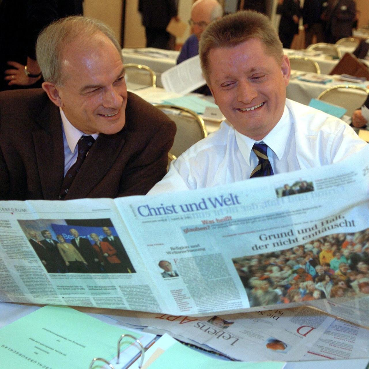 Zwei Männer sitzen an einem Tisch und bleick gemeinsam in eine aufgeschlagene Tageszeitung. Es handelt sich um die Zeitung "Christ und Welt". Das Foto stamm aus dem Jahr 2004.