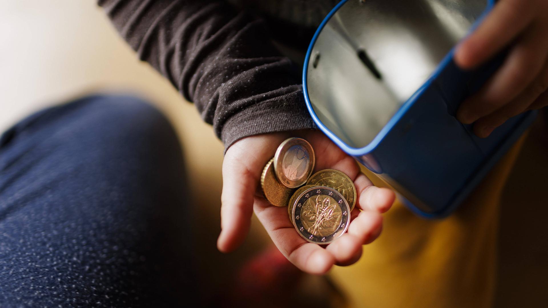 Geldmünzen in einer Kinderhand und eine Blechdose