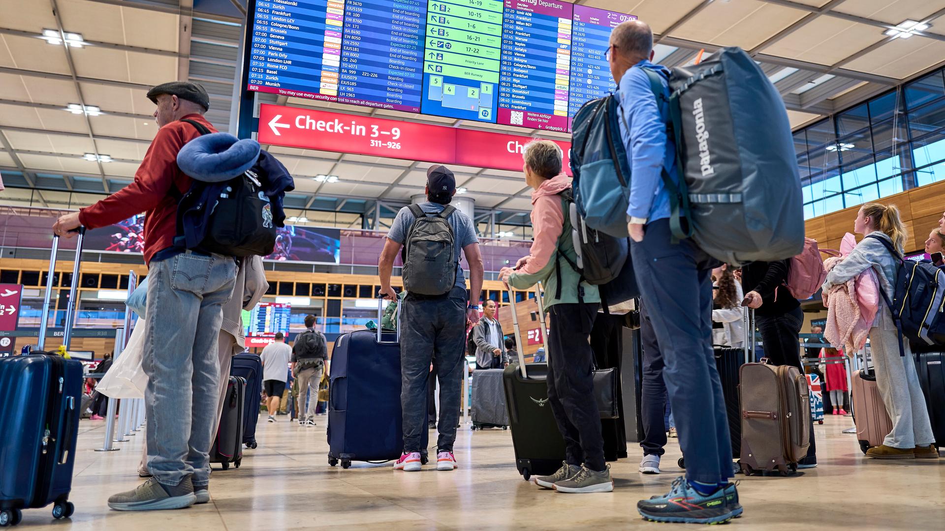 Fluggäste mit Gepäck informieren sich an den Abflugtafeln im Terminal 1 des Flughafens Berlin Brandenburg. 
