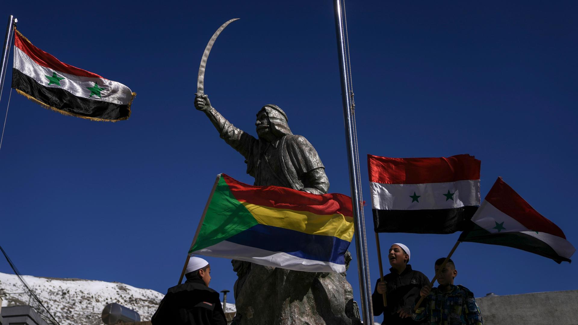 Syrische und drusische Flaggen wehen an einer Kämpferstatue in Golan.