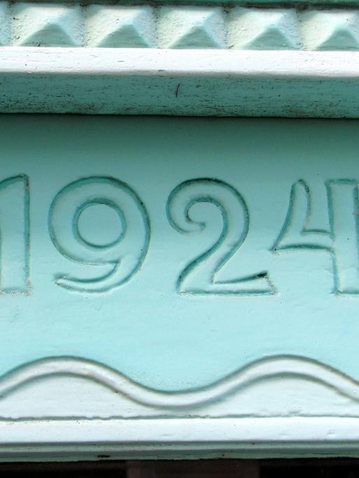Eine mintgrüne Hausfassade zeigt die Jahreszahl 1924.