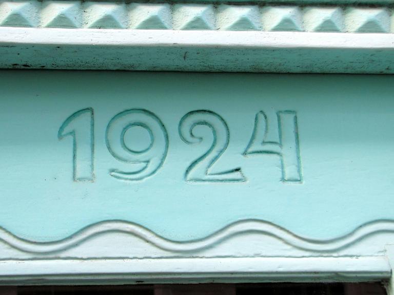 Eine mintgrüne Hausfassade zeigt die Jahreszahl 1924.