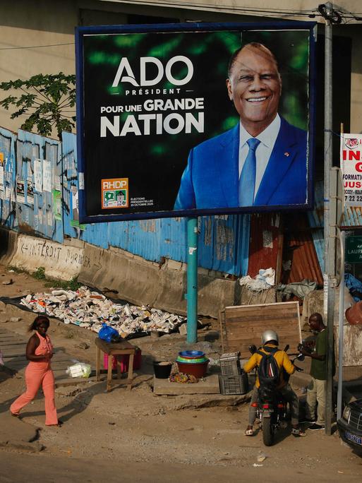 Menschen gehen an einer Wahlkampfanzeige des Präsidenten der Elfenbeinküste, Alassane Ouattara, vorbei. Die Elfenbeinküste wird am 25. Oktober 2025 Präsidentschaftswahlen abhalten.