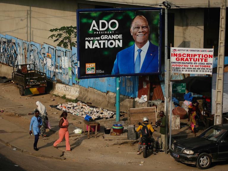 Menschen gehen an einer Wahlkampfanzeige des Präsidenten der Elfenbeinküste, Alassane Ouattara, vorbei. Die Elfenbeinküste wird am 25. Oktober 2025 Präsidentschaftswahlen abhalten.