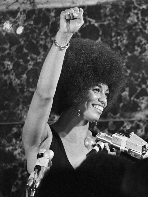 Schwarz-weiß-Aufnahme von 1972: Angela Davis steht neben einem afroamerikanischen Mann auf einer Bühne und reckt die Faust zum Gruß der Black-Power-Bewegung.