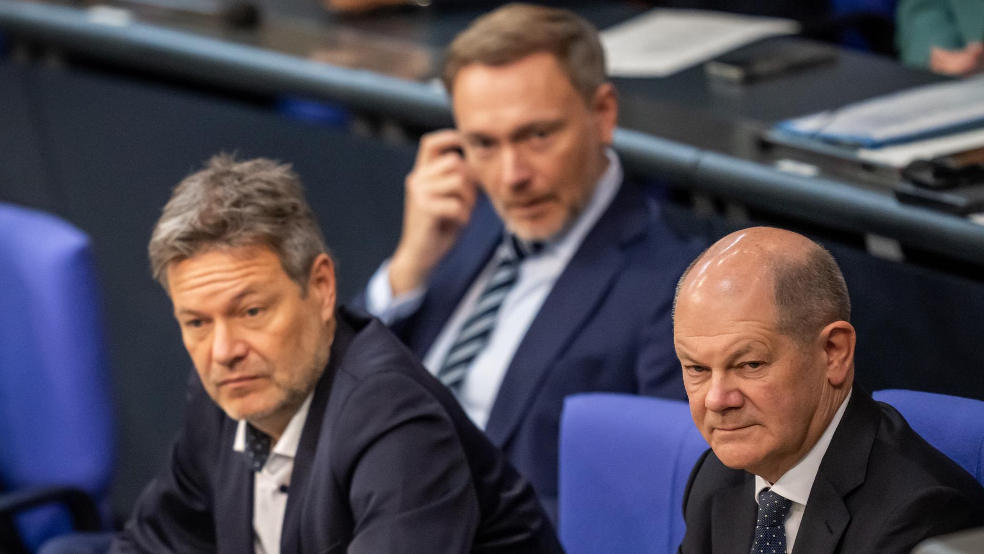 Bundeskanzler Olaf Scholz sitzt rechts neben Bundeswirtschaftsminister Robert Habeck und eine Reihe vor Bundesfinanzminister Christian Lindner im Bundestag.  