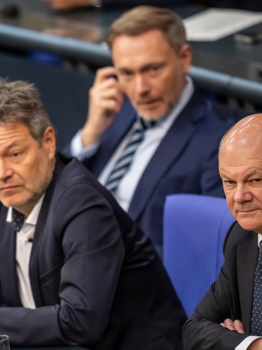 Bundeskanzler Olaf Scholz sitzt rechts neben Bundeswirtschaftsminister Robert Habeck und eine Reihe vor Bundesfinanzminister Christian Lindner im Bundestag.  