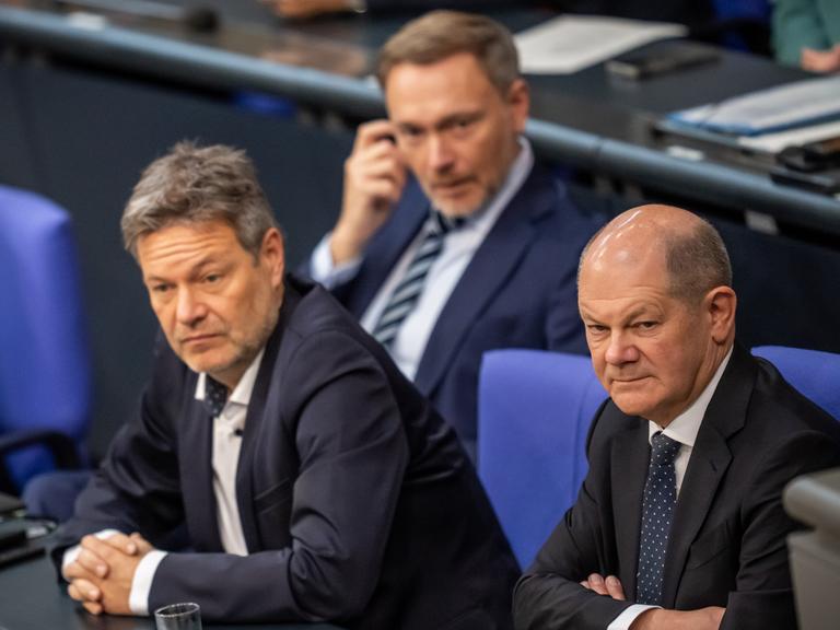 Bundeskanzler Olaf Scholz sitzt rechts neben Bundeswirtschaftsminister Robert Habeck und eine Reihe vor Bundesfinanzminister Christian Lindner im Bundestag.  