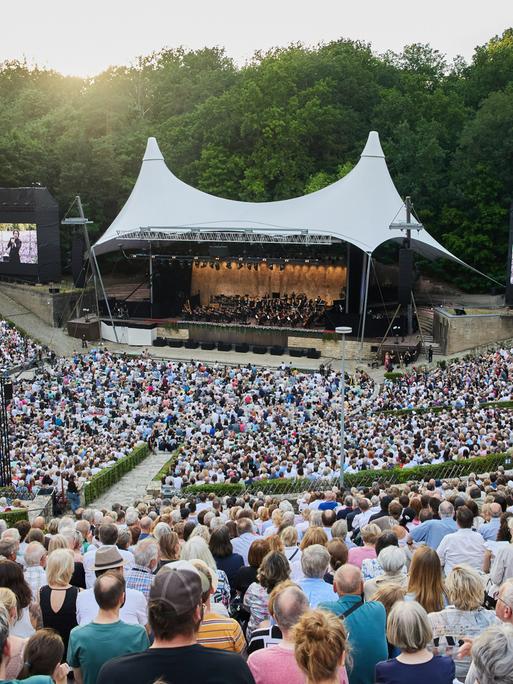 Hunderte Zuschauer hören ein Konzert openair in der Berliner Waldbühne, auf dem Podium spielt ein Orchester.