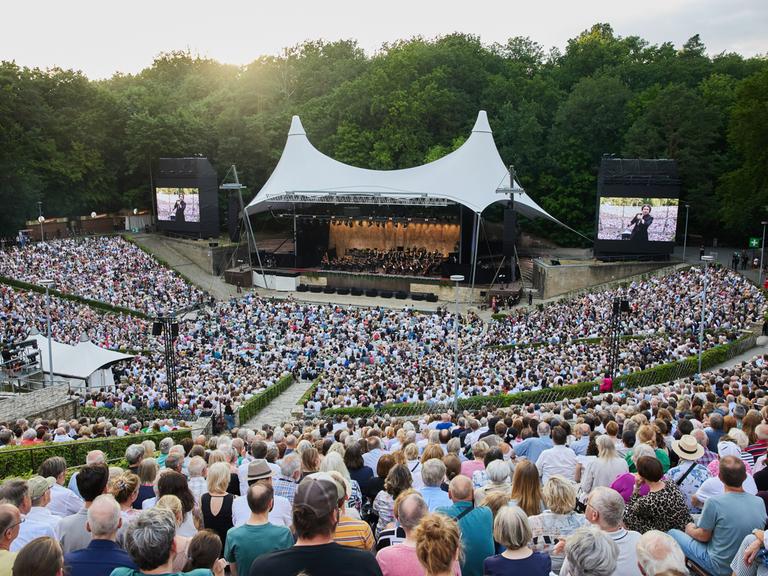 Hunderte Zuschauer hören ein Konzert openair in der Berliner Waldbühne, auf dem Podium spielt ein Orchester.